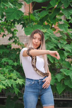 Young woman holding a python snake in an abandoned urban environment, wild concept