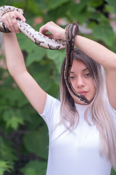 Young woman holding a python snake in an abandoned urban environment, wild concept