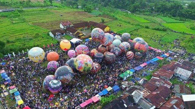 Multiple hot air balloons floating above a busy outdoor event. Scenic countryside festival with vibrant visuals and crowd activity. Wonosobo balloon festival, Indonesia.