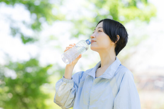 新緑の屋外で水分補給をする女性の横顔ポートレート　運動やスポーツの間にペットボトルの水を飲むクローズアップ