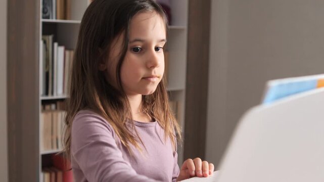 Young girl focusing on playing a digital piano, practicing musical skills and developing her creativity in a home environment with a bookshelf background