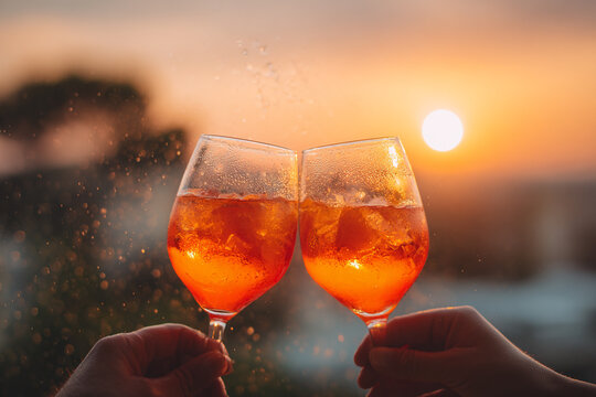 Two Hands Holding Orange Cocktail Glasses Cheering at Sunset Outdoors