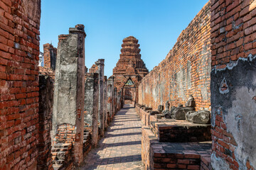 Fototapeta premium Perimeter walkway in the ancient royal palace Wat Prasat Nakhon Luang, in Ayutthaya, Thailand. Row of stone Buddha statues on the right. 