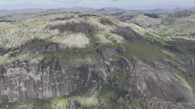 Drone orbits to right as clouds cast shadows on face of summit on a sunny day at Sibebe Rock near Mbabane, Eswatini