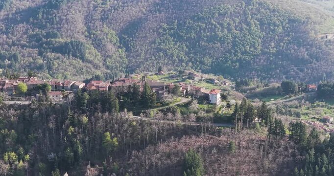 Aerial view of the small stone village of Trappola perched on a ridge surrounded by dense green forests and rolling hills in the Pratomagno area, Trappola, Tuscany, Italy.