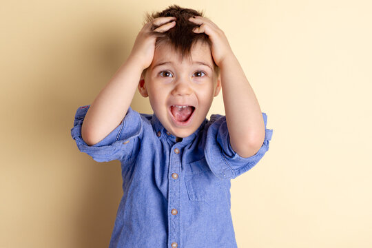 Boy of three years in a blue shirt on a yellow background. Emotional portrait.