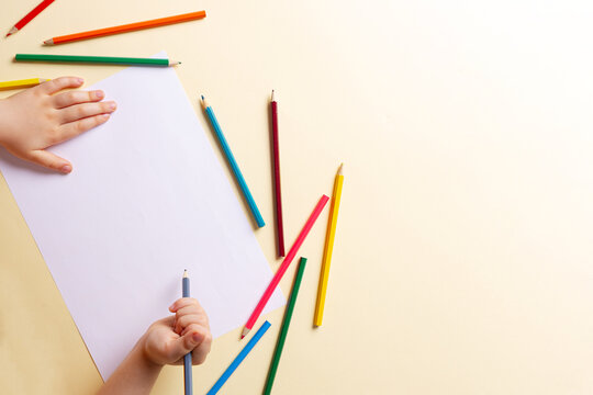 A boy draws with colored pencils on white paper.