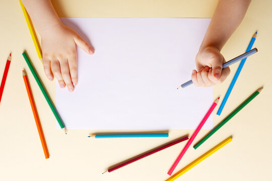 A boy draws with colored pencils on white paper.