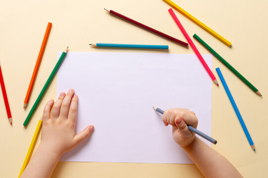 A boy draws with colored pencils on white paper.