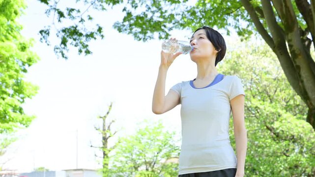新緑の屋外で水分補給をする女性の横顔ポートレート　ウォーキングやランニングの運動やスポーツの間にペットボトルの水を飲むクローズアップ　春夏の半袖の動画　スローモーション