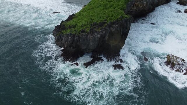 Aerial view of a lush green rocky islet surrounded by powerful ocean waves crashing dramatically against the cliffs.