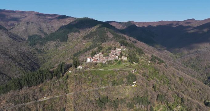 Aerial view of the historic village of Trappola nestled on a mountain ridge surrounded by dense forests and rolling hills under a clear blue sky in Trappola, Tuscany, Italy.