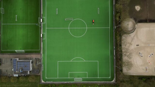 Top down aerial view of tractor mowing and preparing green football pitch