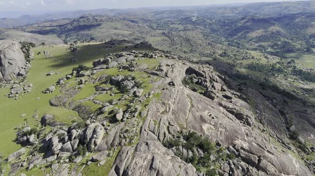 Drone orbits to the left high over Sibebe Rock summit as a large cloud casts a shadow on the cliff face on a sunny afternoon near Mbabane, Eswatini