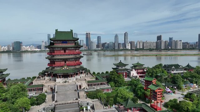 Aerial drone view Nanchang Tengwang Pavilion standing prominently by the Gan River, featuring traditional architecture with a modern city skyline backdrop under a clear sky