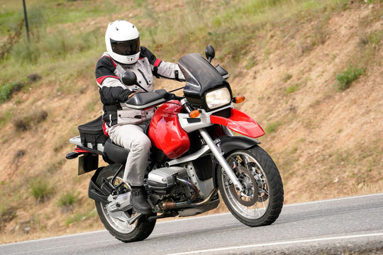 Motociclista conduciendo una moto de aventura BMW R 1100 GS roja en una carretera de monta&ntilde;a
