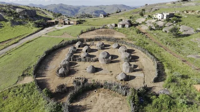Drone flies north over Swazi traditional cultural village toward green valley on late afternoon at Sibebe Rock near Mbabane, Eswatini