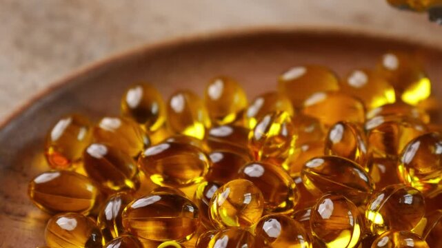 Golden yellow fish oil omega-3 supplement softgel capsules piled on wooden plate, health nutrition vitamin dietary supplement concept