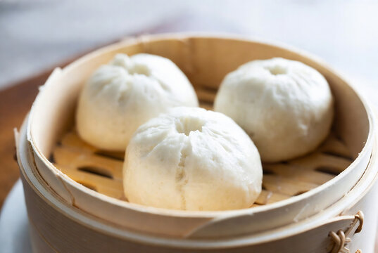 Three steamed bao buns are presented in a bamboo steamer.