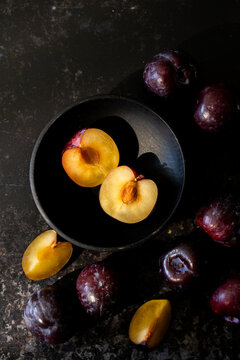 Plums in a black wood bowl on a dark surface 