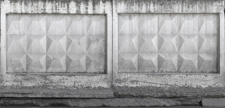 Weathered concrete fence featuring geometric relief panels and repeating textured pattern in monochrome. Urban architectural facade shows stains, decay and strong symmetry ideal for design backgrounds