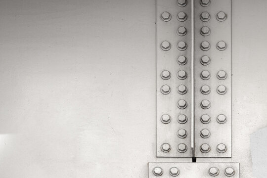 Riveted steel plates and hex bolts create a geometric, industrial composition with worn metal texture and neutral tones, ideal for architecture, engineering, backgrounds, and minimalist themes