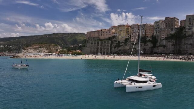 Drone orbit around catamaran with Tropea town in background, Calabria, Italy