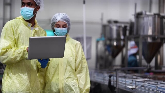 Diverse industrial professionals in protective suits and masks collaborating on technical data and operational audits in a modern smart factory facility.