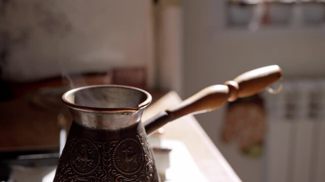 Steam rises from a hot traditional copper coffee pot sitting on a kitchen stove. The backlit vapor creates a cozy morning atmosphere.