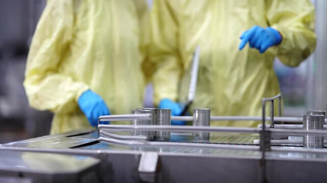 A quality assurance specialist in a yellow protective suit recording data while auditing an automated canning production line in a modern food manufacturing plant.