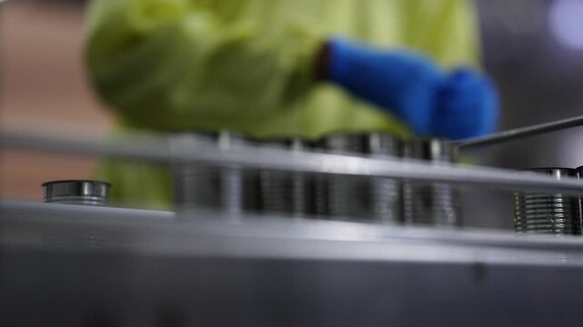 A quality assurance specialist in a yellow protective suit recording data while auditing an automated canning production line in a modern food manufacturing plant.