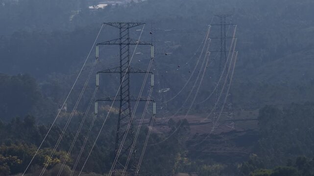 Aerial view of power lines stretching across a landscape, contrasting the industrial structures with the natural terrain, Valongo, Portugal.