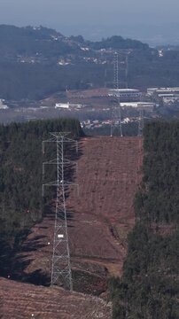 Aerial view of high voltage power lines cutting through a forest, contrasting dark green trees with the cleared brown earth, Valongo, Portugal.
