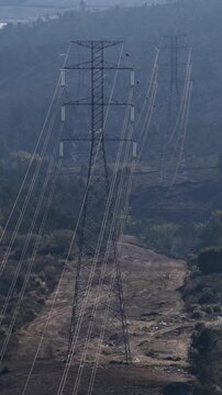Aerial view of tall electric pylons cutting through the landscape with trees, creating a stark contrast against the sky, Valongo, Portugal.