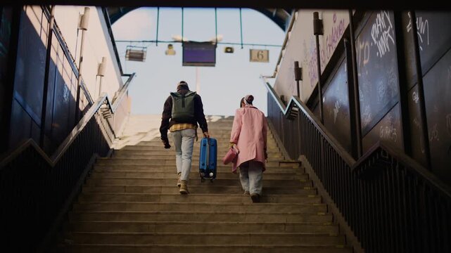 Two tourists ascend a long flight of stairs, carrying luggage through an urban setting. A pair of travelers makes their way up city steps, ready for a journey.