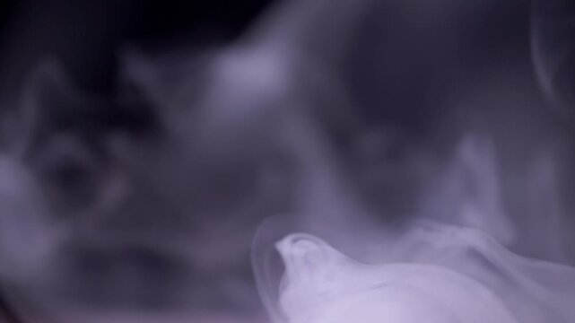 Thick white smoke plumes rise and swirl gracefully, dissipating slowly against a stark black background. Concept of mystery, vaping culture, air pollution, and spooky halloween atmosphere.