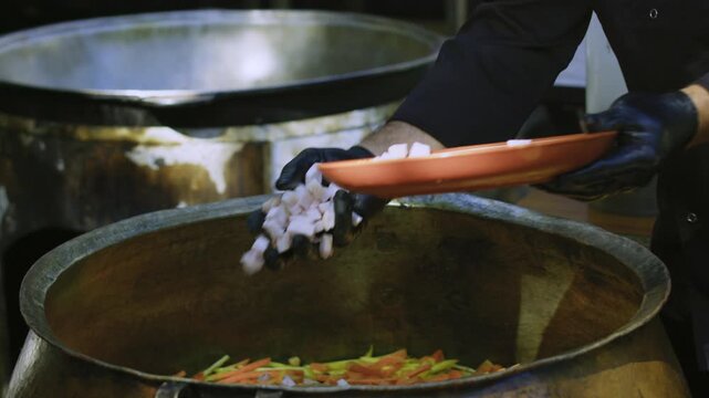 Close-up of chef hand adding fat pieces to Uzbek plov in large ancient kazan