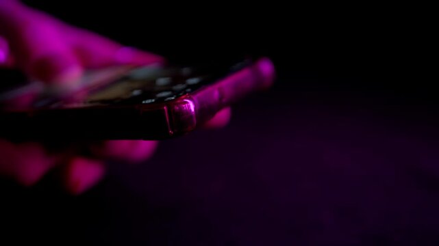 Hands hold a mobile phone illuminated by flashing red and blue strobe lights in the darkness. Concept of contacting emergency services, recording a crime scene, or reporting an accident.
