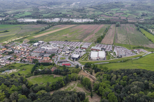 Aerial view of an industrial complex and luxury outlet buildings surrounded by green fields and rolling hills in Leccio, Tuscany, Italy.