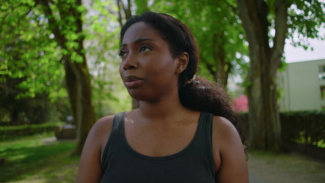 African American woman standing in park holding her head and showing visible stress, worry and preoccupation creating tense and emotionally charged outdoor lifestyle moment in natural environment