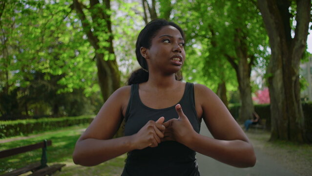 African American woman standing in park holding her head and showing visible stress, worry and preoccupation creating tense and emotionally charged outdoor lifestyle moment in natural environment