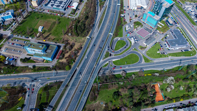 Aerial view of a highway interchange cutting through green spaces and connecting buildings, with cars moving along the roads, Prague, Prague, Czechia.