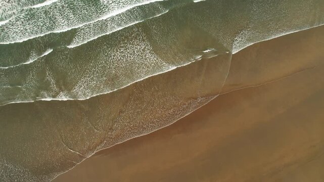 Aerial view of gentle ocean waves meeting the sandy shore