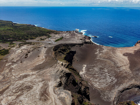 Aerial view of the stark, volcanic landscape meets the vast, deep blue Atlantic ocean, a contrast of raw earth and boundless sea, Capelo, Acores, Portugal.