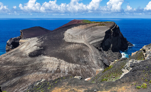 Aerial view of the volcanic landscape of Capelinhos, where black earth meets the azure sea, creating a stark contrast under a bright sky, Capelo, Acores, Portugal.