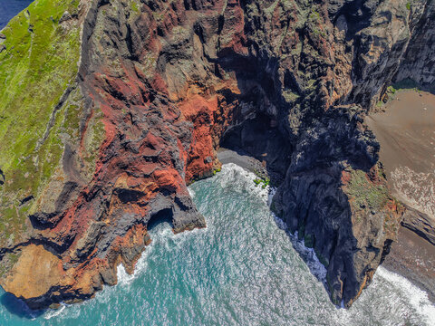 Aerial view of rugged cliffs meet the turquoise sea, a striking contrast of red rock and blue water at Capelinhos Volcano, Capelo, Acores, Portugal.