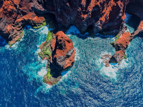 Aerial view of rugged, rust-colored cliffs meet the turquoise sea, creating a striking contrast of textures and tones, Capelo, Acores, Portugal.
