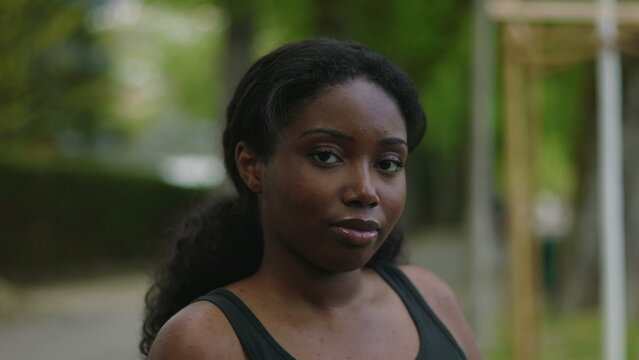 African American woman seated on park bench looking directly at camera with calm and composed expression creating intimate and natural outdoor portrait moment in green environment