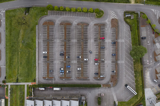 Aerial view of a structured parking lot with several cars parked in rows surrounded by green grass and trees in Leccio, Tuscany, Italy.