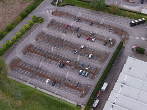Aerial view of a large outdoor parking lot with cars parked in rows next to an industrial building and green trees Leccio, Tuscany, Italy.